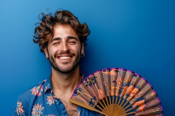 A man with a mustache and beard is smiling and holding a fan. Summer heat concept - obrazy, fototapety, plakaty