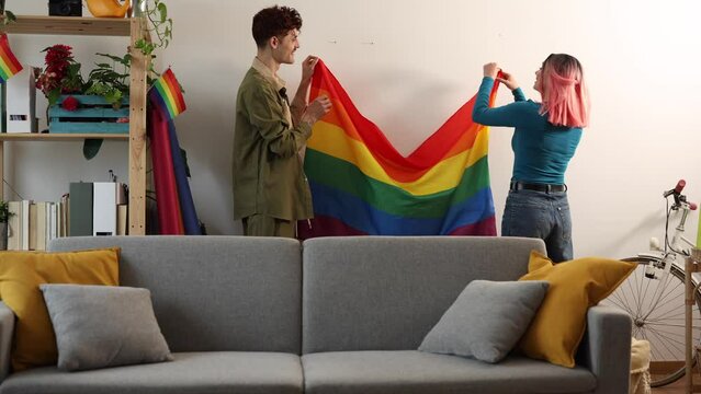 diverse friends placing rainbow flag on wall - preparing lgbt gay pride party