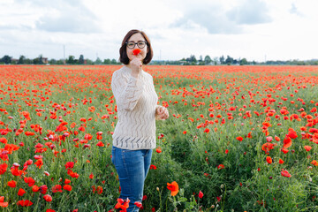 dark haired woman standing in the poppy field holding flower in her hand