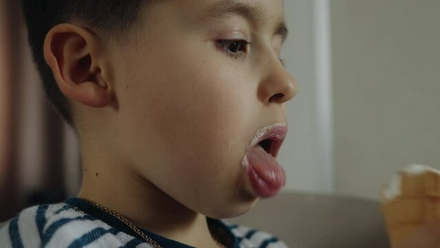 Close up view of a little boy kid holding ice cream in hands, licking with tongue. Delicious dessert