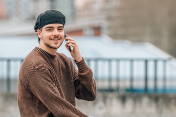 portrait of young man with mobile phone outdoors on the street wearing urban style cap - 785745075