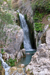 Secluded waterfall cascades into a serene rock pool, a hidden gem tucked away in a lush Spain mountain ravine.