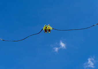 Two thrill-loving friends in a yellow sling soar high into a blue sky with clouds. In a playground during a spring day in Italy.