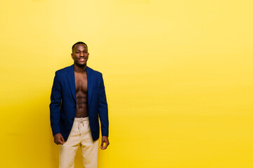 A man in electric blue blazer and white pants poses in front of yellow wall - obrazy, fototapety, plakaty