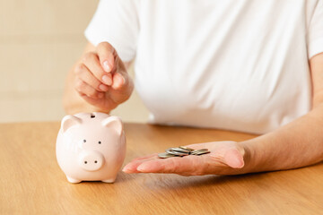 Obraz na płótnie Canvas Saving money investment for future. Senior adult mature woman hands putting money coin in piggy bank. Old grandmother counting saving money planning retirement budget. Investment banking concept