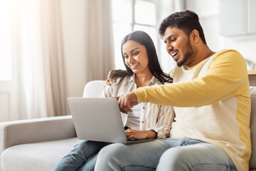 Engaged Indian couple looking at laptop home