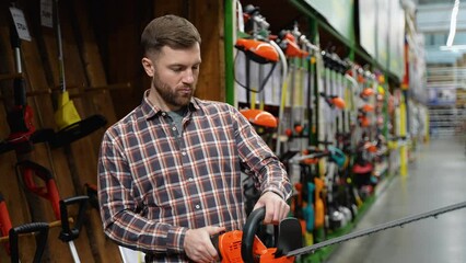 A man in a hardware store chooses a new electric hedge trimmer. Gardening equipment theme