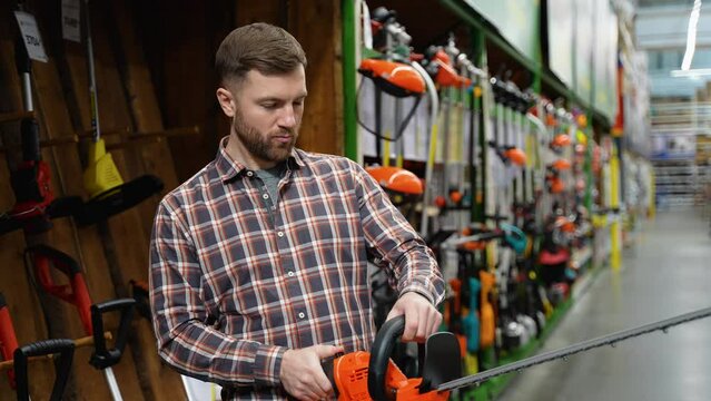 A man in a hardware store chooses a new electric hedge trimmer. Gardening equipment theme