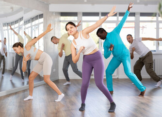 Fototapeta premium Expressive young Asian woman honing hip-hop dance moves in mirrored choreographic studio setting during group training..