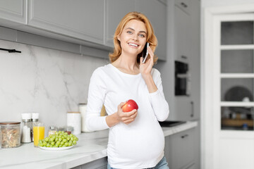 Joyful pregnant lady talking on phone in kitchen