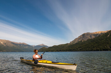 Woman enjoys the scenery of the lake and mountains while sightseeing kayaking on the lakes of Bariloche in Patagonia Argentina during her vacation.