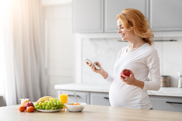 Smiling pregnant woman using smartphone in kitchen