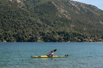 Woman practices kayak on the lakes of Bariloche during her summer vacation. While she enjoys the landscape of mountains and forests.
