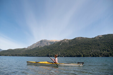 Woman practices kayak on the lakes of Bariloche during her summer vacation. While she enjoys the landscape of mountains and forests.