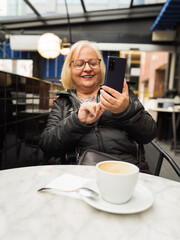 pov senior happy woman enjoying with the cell phone with the coffees already finished - 785760643