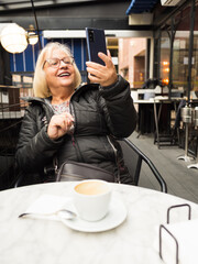 pov senior woman laughing watching selfie with cell phone with already finished coffees - 785760801