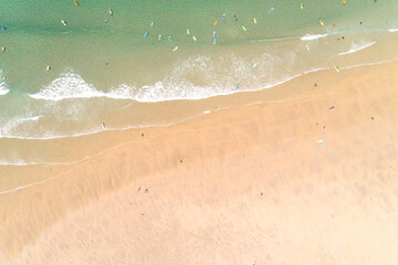 aerial drone top view of a beach, people walking on the sand and surfers with their surfboards in the turquoise water.