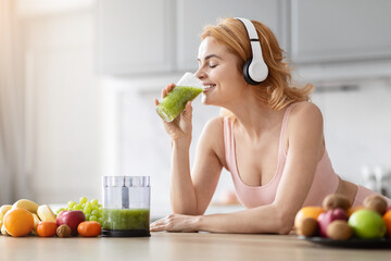 Pregnant woman enjoying smoothie in kitchen, listening to music