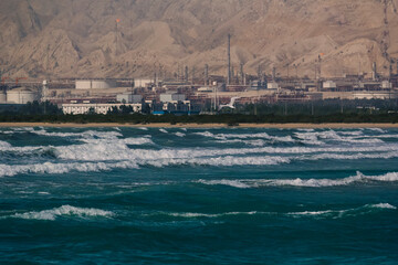 Seascape of blue waves with a background of a refinery complex in southern province of Bushehr, Iran