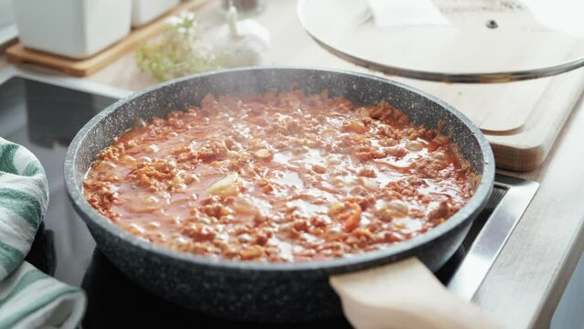 Cooking bolognese sauce in a frying pan on the stove in the kitchen, stock footage video 4k