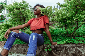 Joven mujer afrodescendiente usa gafas de sol rodeada de plantas y usando ropa urbana