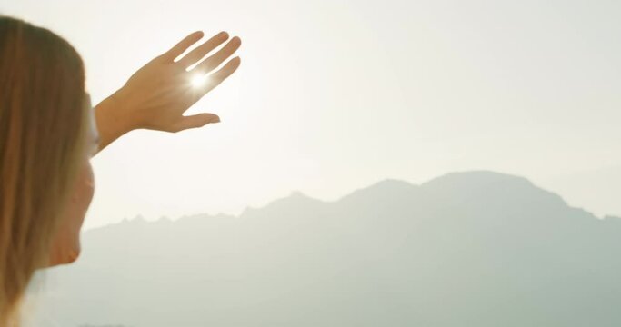 A woman shields her eyes from the sun, gazing towards the hazy mountains. The gesture captures the warmth and brightness of the landscape around her.