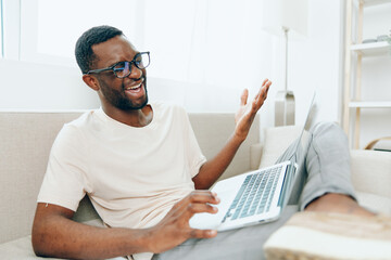Smiling African American Freelancer Working on Laptop on Sofa in Modern Living Room