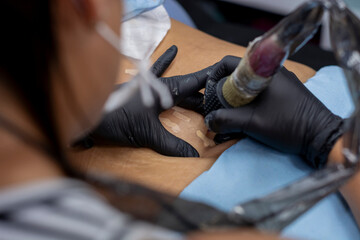 Close-up of the hands of a woman who is tattooing the stretch marks on a woman's skin - Powered by Adobe