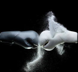 Grey Boxing two glove hit sand together and explode. White Boxer glove impact particle sand splash as exercise training. Black background isolated