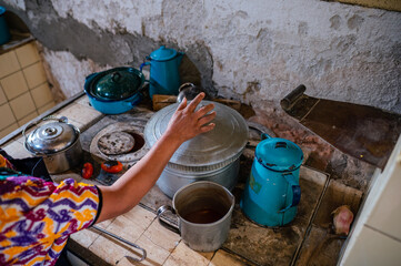 A woman's hand lifts the lid of the pot where the tamales are cooked.