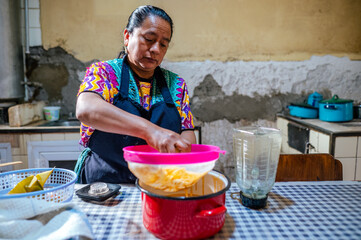 Latina woman of the Mayan ethnic group processes a sauce and uses a plastic filter to improve the...