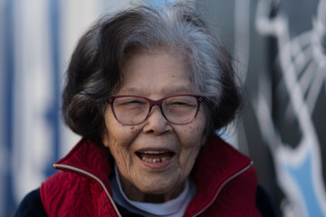 An elderly grandmother lets out a big laugh while dining outdoors. She is over ninety years old, of...