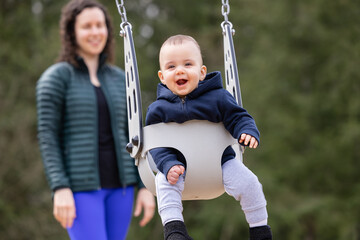 Caucasian Baby Boy on a swing with mother. Park Outside.