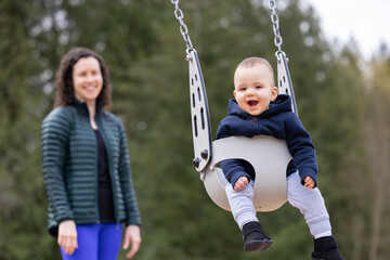 Caucasian Baby Boy on a swing with mother. Park Outside.
