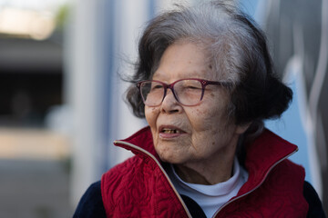 An elder grandmother over ninety years old turns to the side, mid-conversation, in a candid photo while sitting outdoors. She is from Okinawa (she is Ryukyuan), a blue zone with high longevity.