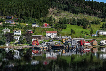 A calm fjord reflects the quaint Kvanne village surrounded by greenery in a Norwegian summer....