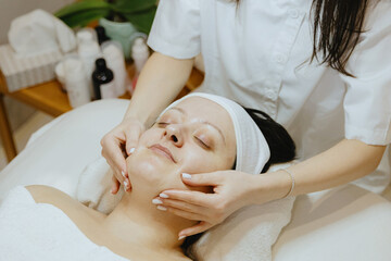 A girl cosmetologist massages the patient s face with her fingers.