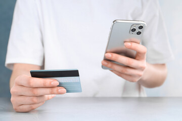 Online payment. Woman with smartphone and credit card at white table, closeup