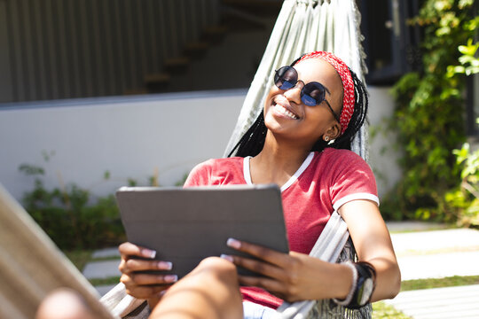 African American young woman relaxing in hammock at home, holding tablet