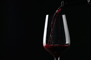 Pouring red wine into glass against black background, closeup. Space for text