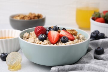 Tasty oatmeal with strawberries, blueberries and walnuts in bowl on grey table