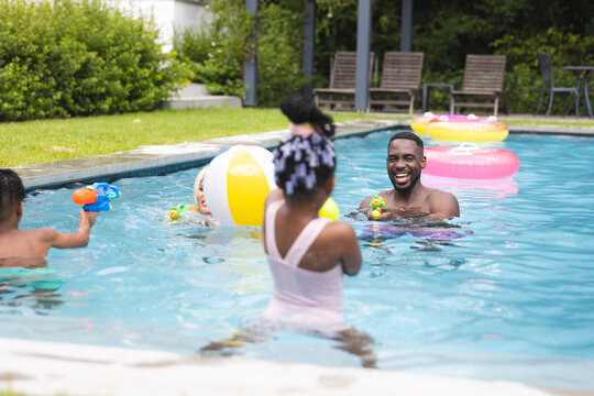 A diverse family enjoying pool time at home, with the father laughing, kids playing, and the mother 