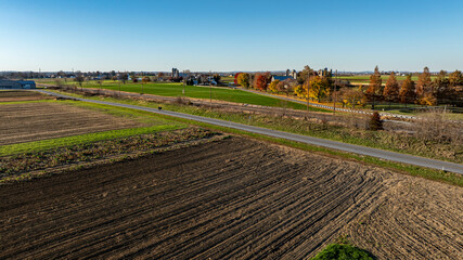 An aerial image captures the textured farmland during autumn, with a country road cutting through,...