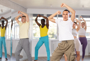 Fototapeta na wymiar Dynamic Asian guy training hip-hop dance poses in dancehall during workout session