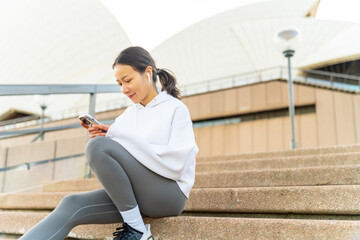 Happy Asian woman listening to music from mobile phone and earphones with mobile app during jogging...