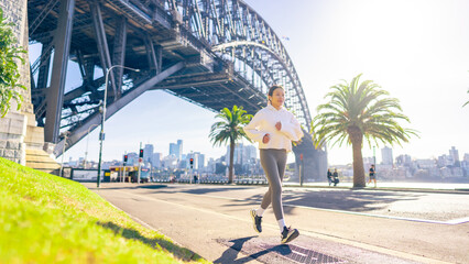 Obraz premium Asian woman in sportswear listening to music with earphones and mobile phone app jogging workout exercise at city street in the morning. Healthy care motivation sport training and running concept.