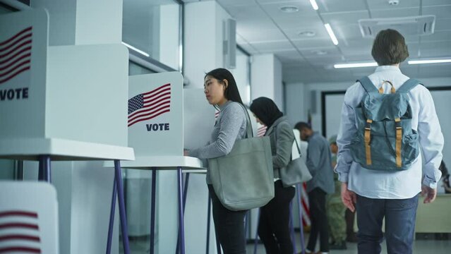 Asian woman comes to voting booths in polling station office. National Election Day in United States. Political races of US presidential candidates. Concept of civic duty and patriotism. Dolly shot.