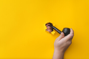 The hand of a young man holds a smoking pipe on a background of yellow paper. Mouth and lips in a...
