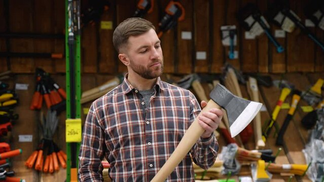 Bearded man lumberjack chooses axe in the hardware store