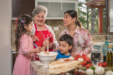 Grandmother with her daughter and grandchildren happily prepare corn tamales. Latin family.